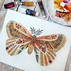 a butterfly is sitting on top of a piece of paper next to some paint and crayons