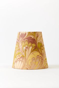 a lamp shade that is on top of a white surface with an abstract design in gold and pink