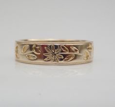 a gold wedding band with flowers and leaves on the side, set against a white background