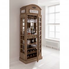 a tall wooden cabinet with wine glasses and bottles on it's shelves in a white room