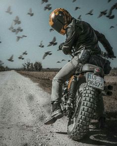 a man riding on the back of a motorcycle down a dirt road surrounded by birds