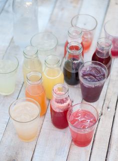 many different colored drinks are lined up on a wooden table with water in the middle