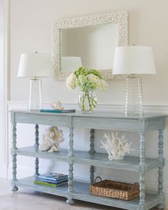 a blue table with two lamps and a mirror on the wall above it, along with a basket of flowers