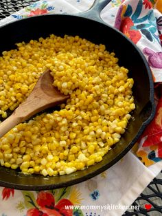 corn is being cooked in a skillet with a wooden spoon on a tablecloth