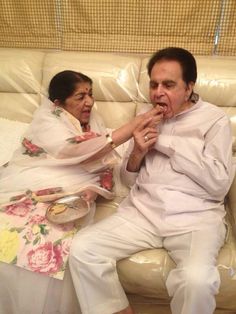 an old man and woman sitting on a couch with food in their hands as they eat