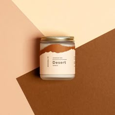 a jar of desert candle sitting on top of a brown and white wall next to a pink and beige background