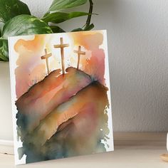 watercolor painting of three crosses on top of a hill with mountains in the background