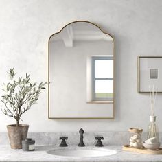 a bathroom with marble counter top and gold framed mirror above the sink, along with two vases filled with plants