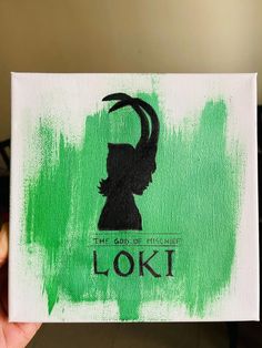 a person holding up a green and white painting with the words loki on it in black