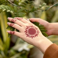 a woman's hand with henna tattoos on her left arm and the other hand holding a plant