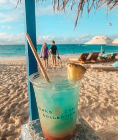 a drink sitting on top of a wooden table next to the ocean with people in the background