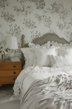 a bed with white sheets and pillows in a bedroom next to a night stand on a dresser