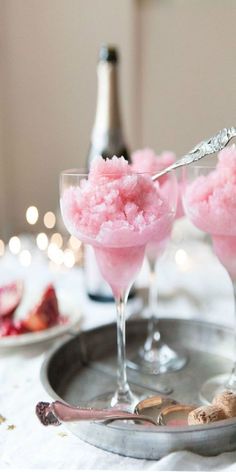 two glasses filled with pink ice cream on top of a silver tray next to wine bottles