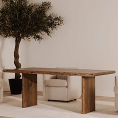 a large wooden table sitting on top of a white rug next to a chair and a tree