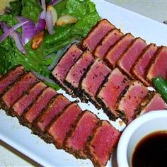 slices of meat and greens on a plate with dipping sauce in a bowl next to it