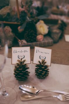 two place cards with pine cones on them are sitting on a table next to silverware