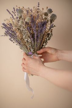 a person holding a bunch of dried flowers in their hands with ribbon tied around them