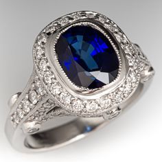 This glimmering ring is centered with one (1) bezel set cushion cut sapphire that is bordered by twenty-one (21) bead set round brilliant cut diamonds. The shoulder and side faces of the ring are set with sixty-eight (68) bead set round brilliant cut diamonds, and six (6) bezel set round brilliant cut diamonds. The ring has milgrain edging.  It measures 12.9mm at the top, rises 7.1mm above the finger, and tapers to 2.5mm wide by 1.5mm thick at the base of the shank. There are a few very light swirls in the platinum at the base of the shank.  The ring is currently a size 4.25. Luxury Cushion Cut Sapphire Diamond Ring, Luxury Lab-created Sapphire Ring For Formal Occasions, Formal Sapphire Ring With Brilliant And Cushion Cut, Formal Sapphire Ring With Cushion Brilliant Cut, Luxury Gia Certified Cushion Cut Sapphire Ring, Formal White Gold Cushion Cut Sapphire Ring, Gia Certified Cushion Cut Sapphire Ring In Platinum, Formal Cushion Cut Sapphire Ring With Diamond, Luxury Sapphire Ring Cushion Cut Brilliant