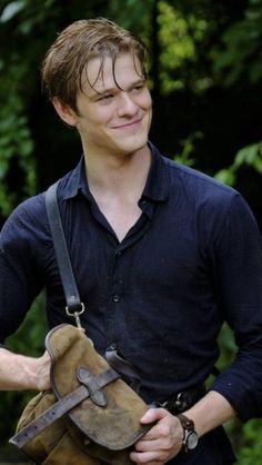 the young man is holding an old leather bag in his right hand and smiling at the camera