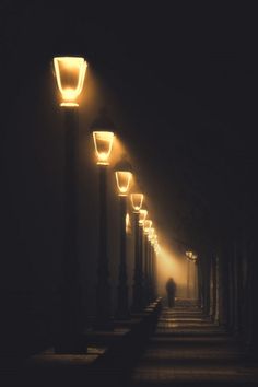 a person is walking down the street at night with some lights shining on them and there are many lamps in the dark