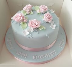 a blue and pink birthday cake in a white box with flowers on the top is shown