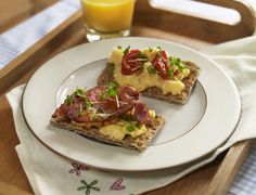 two pieces of toast with ham and vegetables on them sitting on a plate next to a glass of orange juice