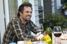 a man sitting at a table with two wine glasses in front of him and smiling