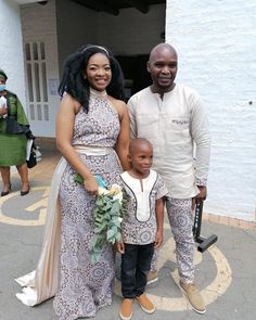 a man and woman standing next to a little boy in front of a white building