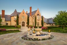 a large house with a fountain in front of it and landscaping around the entrance area