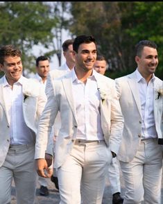 a group of men in white tuxedos walking down the street with each other