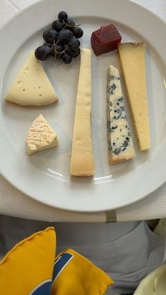 a white plate topped with different types of cheeses and fruit on top of a table