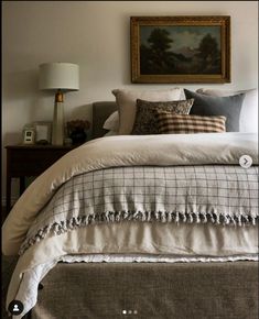 a bed with white sheets and pillows in a bedroom next to a painting on the wall