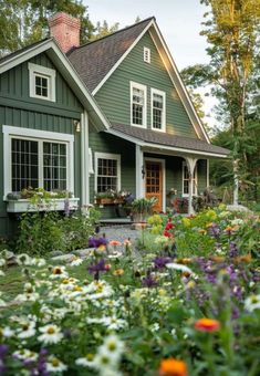 a green house with lots of flowers in the front yard and windows on each side