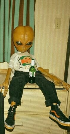 an alien doll sitting on top of a dresser next to a bottle and suitcases