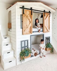 two children are sitting on the roof of a doll house with wooden doors and windows