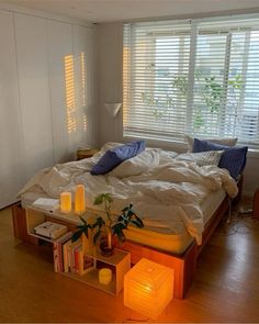 a bed with white sheets and blue pillows in a bedroom next to a window filled with books