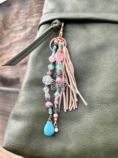 a green purse with a tassel hanging from it's side and some charms attached to the handle