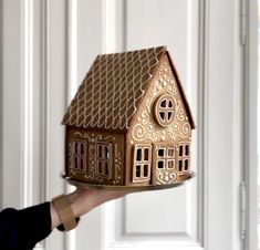 a person holding a small house shaped cake on top of a plate in front of a door