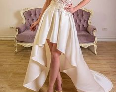 a woman in a white dress standing on a wooden floor next to a purple couch