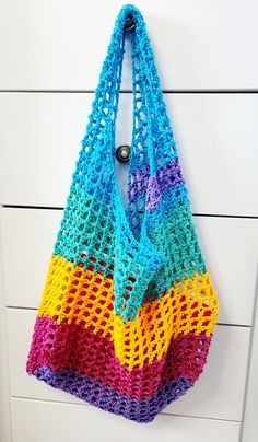 a multicolored crocheted bag hanging on a white cabinet door with handles