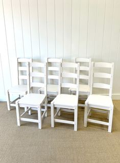 six white wooden chairs sitting in a row on the floor next to eachother