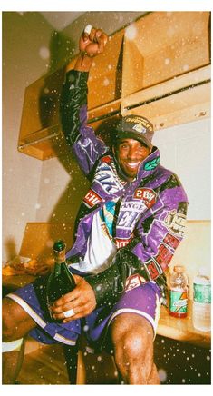 a man sitting on top of a kitchen counter next to a wooden shelf filled with bottles