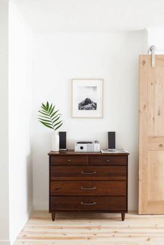 a wooden dresser sitting next to a door in a room with white walls and wood floors