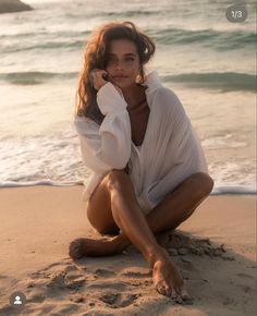 a woman sitting on top of a sandy beach next to the ocean