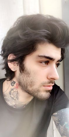 a man with long black hair and piercings on his face looking out the window