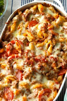 a casserole dish with meat, cheese and tomato sauce on the side next to salad