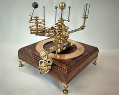 an antique clock with brass parts and pendulums on it's stand, sitting on a white surface