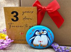 there is a blue button with two penguins on it next to a card and flowers