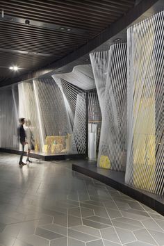 two people are walking through an empty subway station with yellow and white lines on the walls