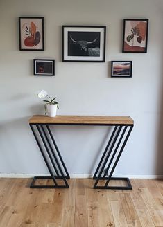 a wooden table sitting in front of a white wall with pictures on the wall above it